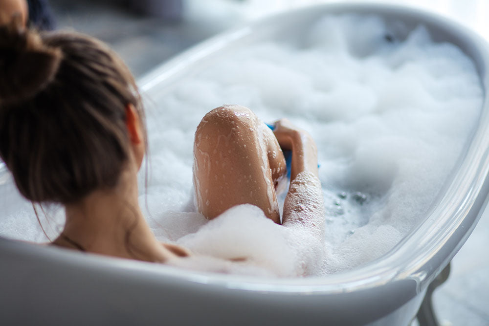 Junge Frau, die in einer Badewanne mit Schaumbad sitzt als Sinnbild für die Nassrasur der Bikinizone